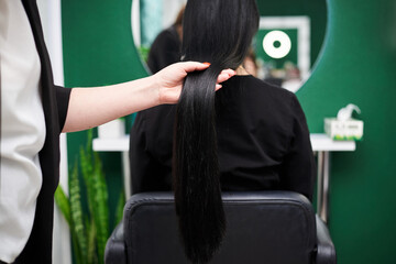 Professional hairdresser making hairstyling for female client in front of mirror. Close-up picture of work process in barber shop. Young brunette woman getting ready for party