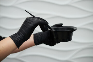 Close-up picture of hairdresser's tools in female hands with black gloves. Process of mixing hair...