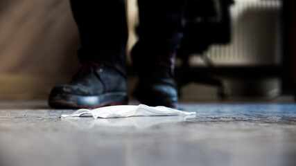 A fallen protective mask on screed floor with somebody  wearing leather boots standing behind in interior shot.