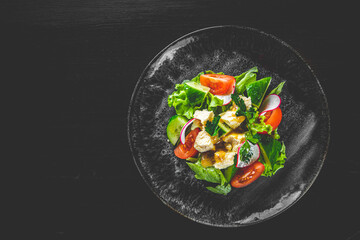 Salad with cucumber, tomato, red onion, pepper, parsley and Feta cheese on black background