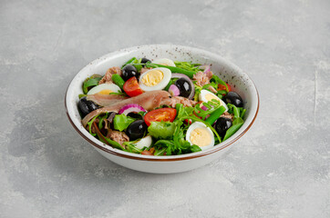 French salad Nicoise with tuna, egg, green beans, tomatoes, olives, lettuce, onions and anchovies on a gray concrete background. Healthy food.