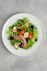 French salad Nicoise with tuna, egg, green beans, tomatoes, olives, lettuce, onions and anchovies on a gray concrete background. Healthy food.