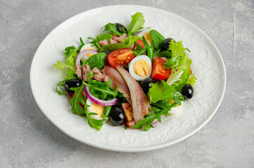 French salad Nicoise with tuna, egg, green beans, tomatoes, olives, lettuce, onions and anchovies on a gray concrete background. Healthy food.