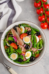 French salad Nicoise with tuna, egg, green beans, tomatoes, olives, lettuce, onions and anchovies on a gray concrete background. Healthy food.