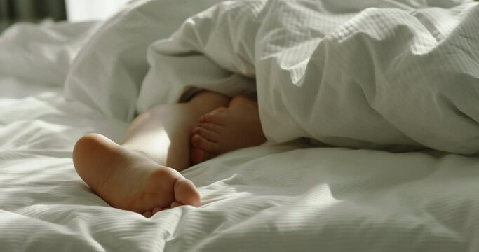 Close up shot of feet of sleeping woman in cozy comfortable bed with white bedding. Healthy sleep on orthopedic matrress 4k footage