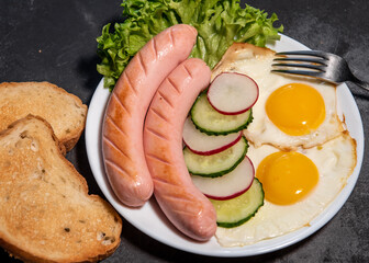 Two fried eggs and sausages, lettuce, cucumber and radish slices on a white plate, toast. Scrambled eggs. Breakfast. Healthy eating. Close-up
