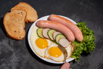 Two fried eggs and sausages, lettuce, cucumber and radish slices on a white plate, toast. Scrambled eggs. Breakfast. Healthy eating. Close-up