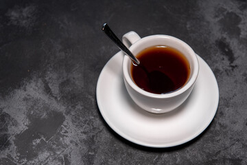 Coffee in a white cup on a saucer on a dark background. A cup of tea or coffee with a spoon. Close-up