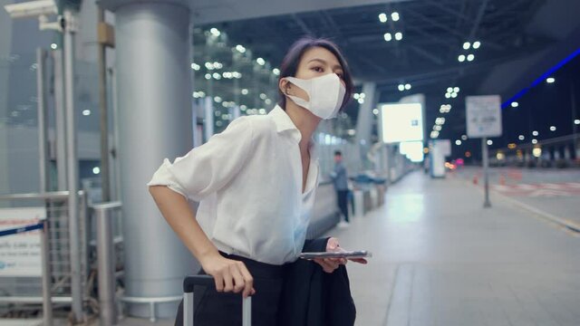 Asian business girl arrive destination wear face mask stand outside look smart phone wait car terminal at domestic airport. Business commuter covid pandemic, Business travel social distancing concept.