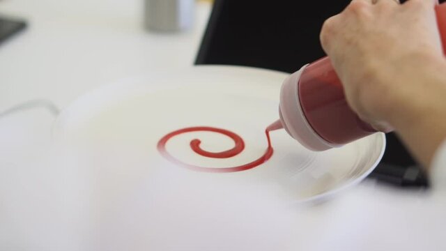 Chef creating spiral design on dessert plate with fruit puree sauce