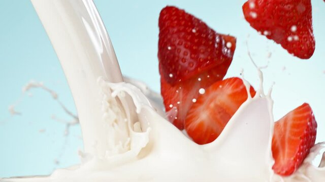 Super slow motion of strawberries falling into cream.