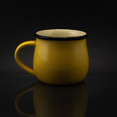Close up of a yellow ceramic mug isolated on a dark background © Cristian Muñoz Gallardo/Wirestock