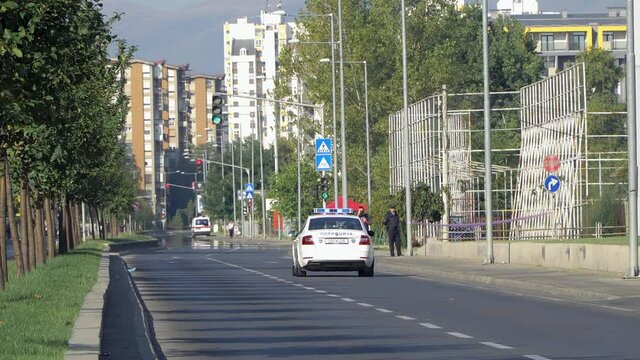 Police car passing on the boulevard in Skopje securing the street with an ambulance in the background