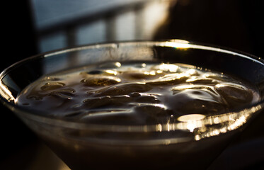Close up detail image of cream alcohol drink on ice in V shaped cocktail glass. Sunset shot outdoors.