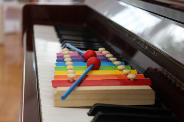 Close up image of a colorful toy xylophone with mallets put on the keyboard of a classical piano.