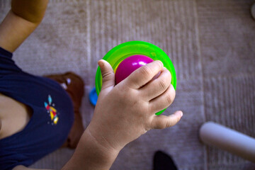 Naklejka premium Top view close up image of a toddler's right hand releasing a purple ball into a green plastic toy with a white carpet on the floor.