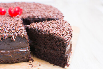 Big Chocolate cake, decorated with chocolate chips and cherry on wooden background