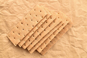 Light brown multi-grain rye crispbread on craft paper, close-up, top view.