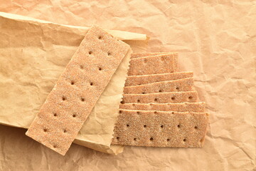 Light brown multi-grain rye crispbread on craft paper, close-up, top view.