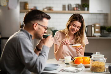 Beautiful woman enjoying in breakfast with her boyfriend. Happy young couple drinking coffee and eating sandwich at home