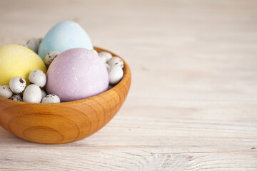 Colorful Easter eggs in a wooden bowl on a wooden background, place for text.