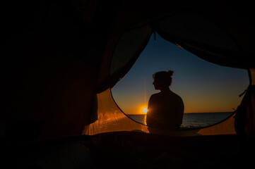 A woman and a dog are resting in a tent in nature at sunset. The girl and Jack Russell Terrier set up camp on the river bank