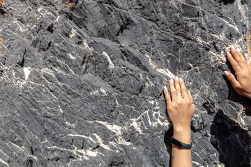 the girl's hands are on a large black granite rock with white flecks of threads. beautiful black natural stove and delicate hands of a girl with a watch