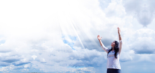 Fototapeta na wymiar A young woman stands with raised hands in the sky. Clouds and blue sky. Praise and Prayer.