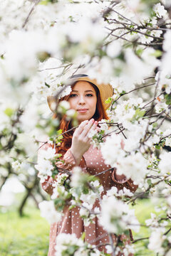 Red-haired girl walks in a spring blooming apple orchard