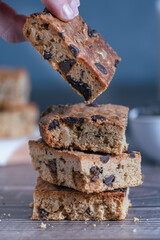 Close up of pile of delicious blondie (brownie) on a dark background. Homemade biscuit.  hand picking a piece of blondie. Vertical..
