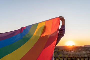 Rainbow LGBT flag concept.Back view unrecognizable woman holding gay pride flag at sunset in countryside.