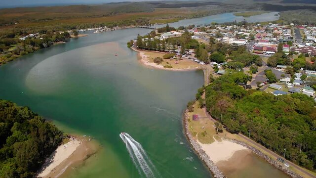 Aerial view of a boat on a river and the Evans Head town, New South Wales, Australia - tilt up, drone shot