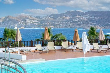 Several closed umbrellas near the pool in Greece. Greek hotel by the sea on the sunny day