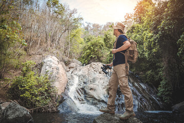 Obraz premium Male hiker with backpack holding binoculars looking waterfall in forest