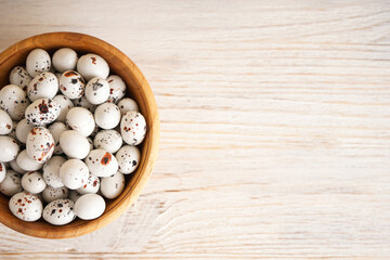 Quail easter eggs in wooden bowl on wooden background, flat lay. Place for text.
