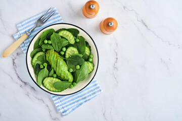 Green vegetable salad with spinach, avocado, green peas and olive oil in bowl on light gray slate, stone or concrete background. Top view with copy space. Green vegetables for diet concept.