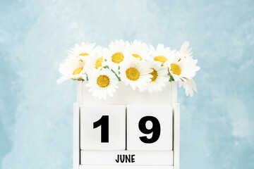 cube calendar for June with daisy flowers over blue with copy space