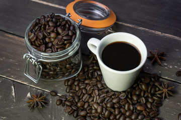 Coffee beans in glass jar with american black coffee cup on old wooden table.Creative cafe concept on rustic background.