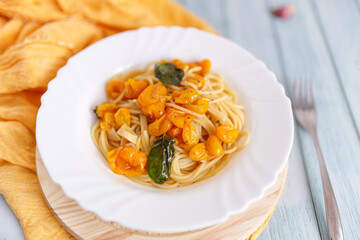 Pasta, spaghetti with yellow tomato in white plate. Blue background. Top view. Close up.