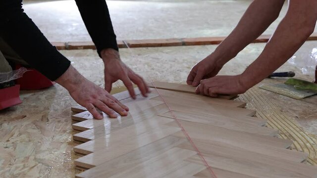 Laying parquet in an apartment during renovation. Herringbone parquet video 4k. Worker installing wood parquet.