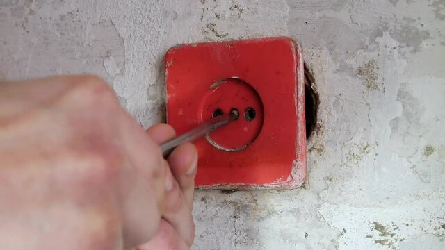 Maintenance repair works renovation in the flat. Restoration indoors. Man is uninstalling old plastic socket  for switches. Holes with wires in the wall.