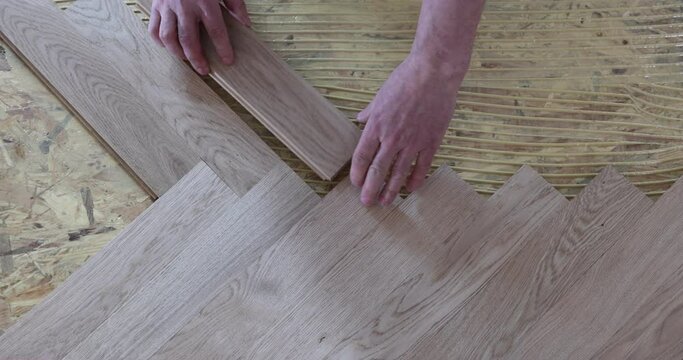 Laying parquet in an apartment during renovation. Herringbone parquet video 4k. Worker installing wood parquet.