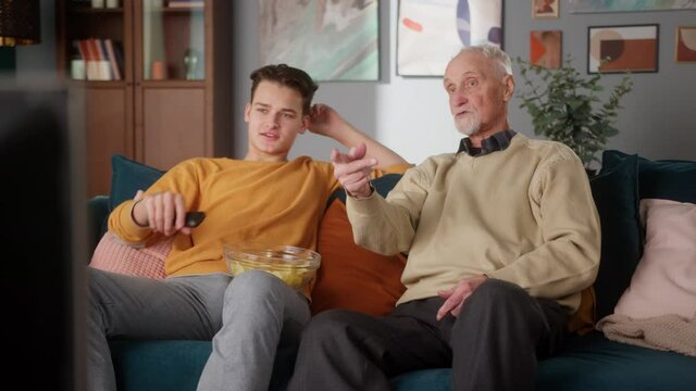 Grandfather and grandson are watching movie with popcorn at table at home. Different generations and modern technologies, old and young man, happy family, grandson on college vacations with gradndpa