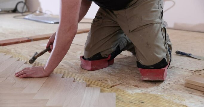 Laying parquet in an apartment during renovation. Herringbone parquet video 4k. Worker installing wood parquet.