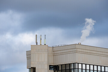 Chimney with white smoke on the roof of a building, generating air pollution. Clouded sky on the background.