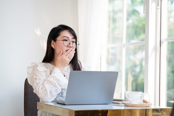 asian freelance business female yawning covering her mouth of courtesy in front of working with laptop computer with coffee cup and smartphone in coffee shop like the background,communication concept