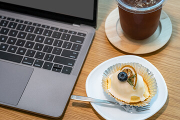 Close-up of ice coffee in cup mug and Homemade white orange cake ​with keyboard  laptop computer on wood desk office desk in coffee shop at the cafe,during business work concep