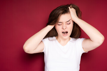 Pretty girl gets annoyed with headache after getting braces. Isolated on red background