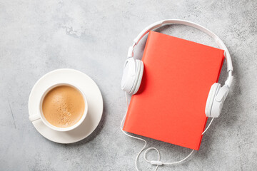 Headphones, book and cup of coffee on concrete surface