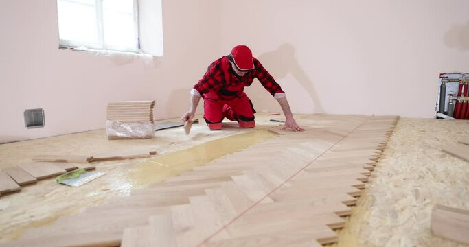 Carpenter worker installing wooden floor, parquet in an apartment during renovation. Worker installing wood parquet. Construction in a renovated room installation of parquet
